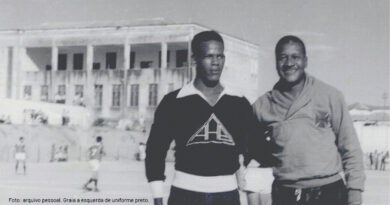 Na imagem: dois homens, em frente a um campo de futebol, o homem do lado esquerdo veste uniforme preto e o do lado direito uniforme branco. A foto está em preto e branco.